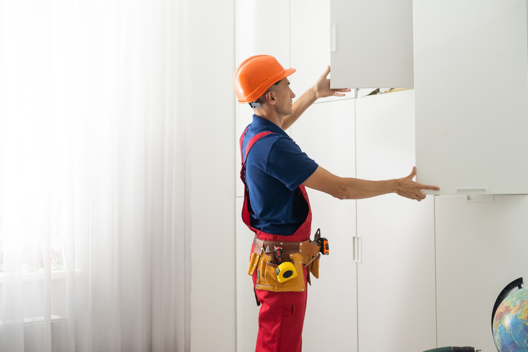 Worker installing a white cabinet in a room.