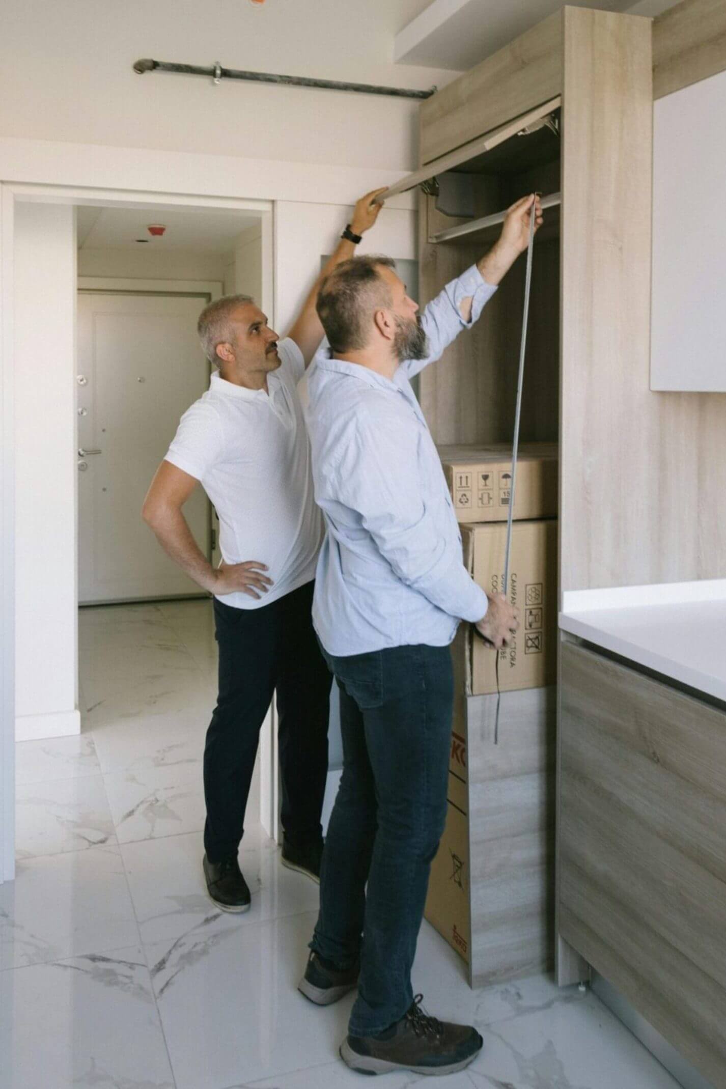 Two men measuring kitchen cabinets with a tape measure.