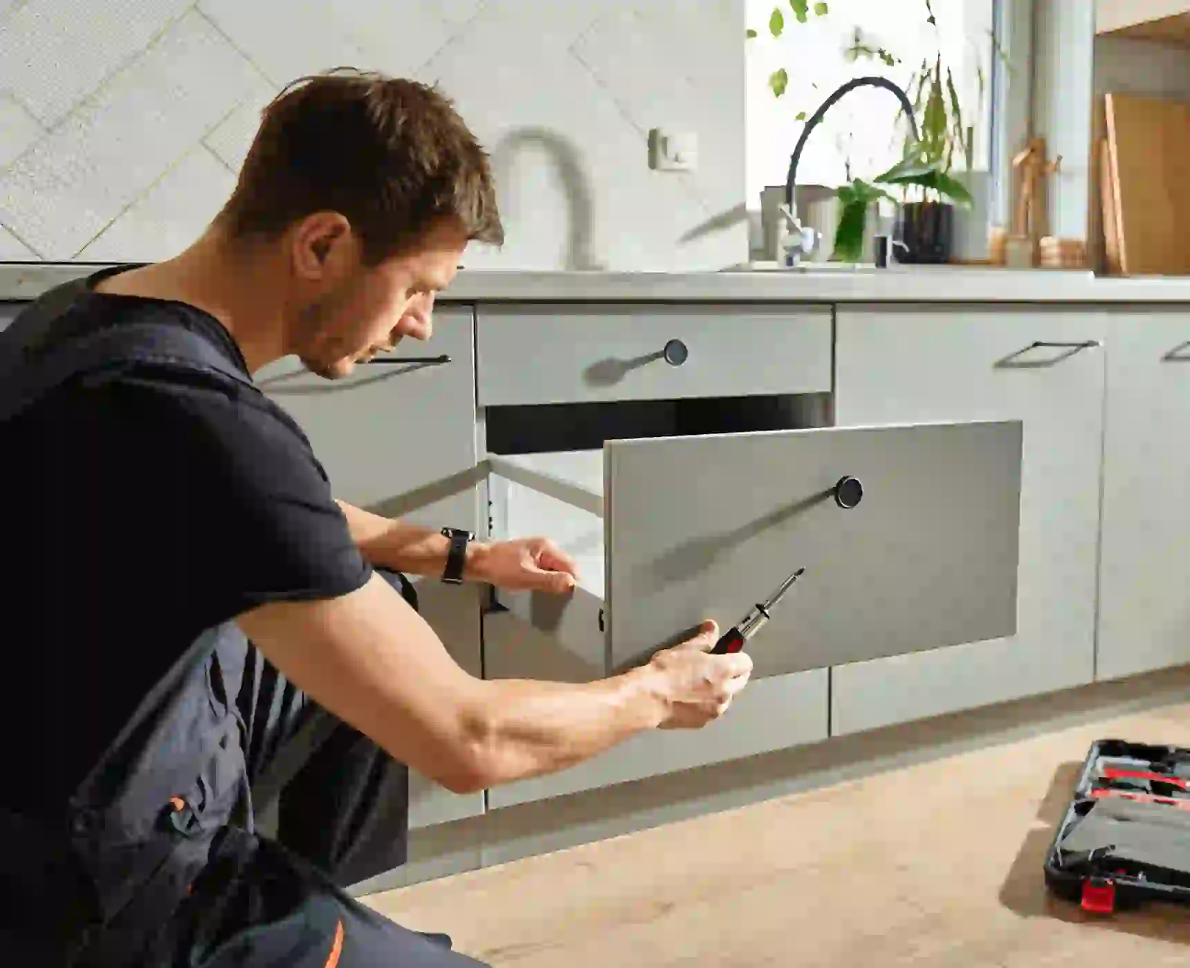 Man repairing kitchen cabinet drawer with screwdriver